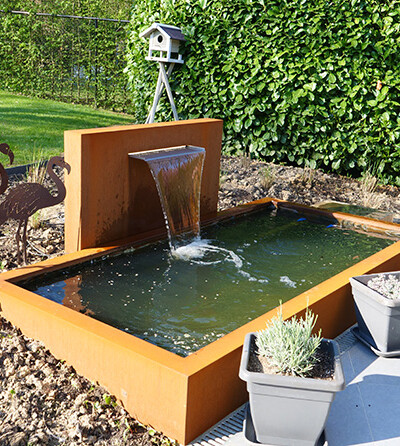 Miroir d'eau en acier Corten avec fontaine, entouré de décorations extérieures de chez Kubik Création