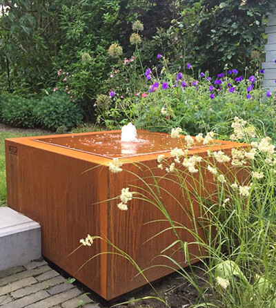 Table d'eau en acier Corten de Kubik Création entourée de fleurs sauvages