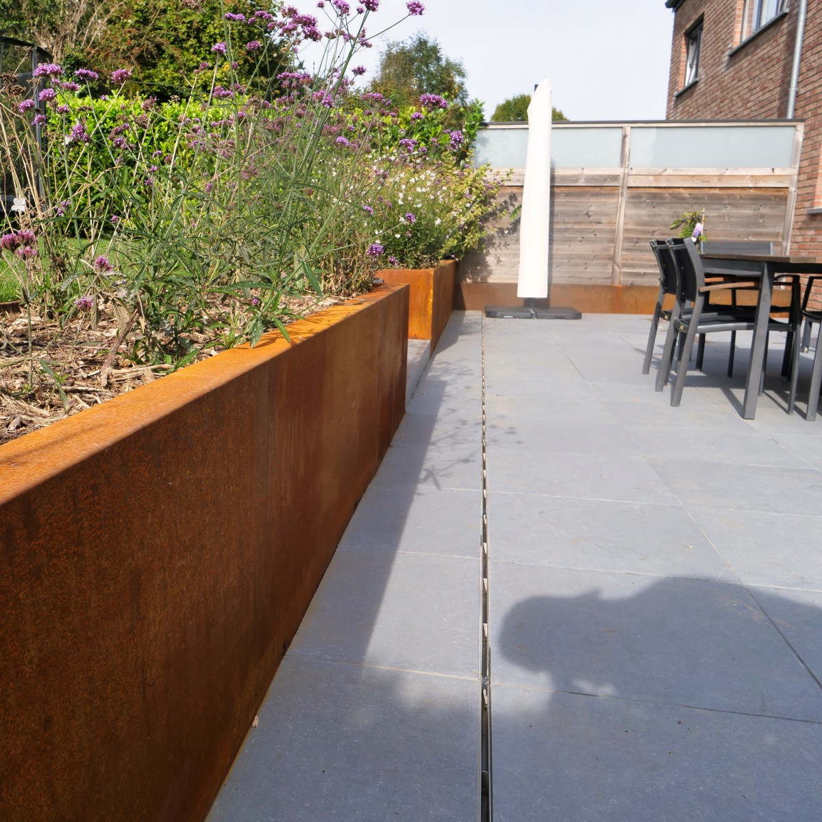 Jardinière en acier Corten fleurie sur une terrasse extérieure en pavés