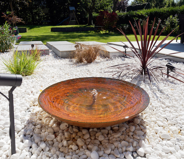 Fontaine en acier Corten de Kubik Création sur galets blancs dans un jardin paysager