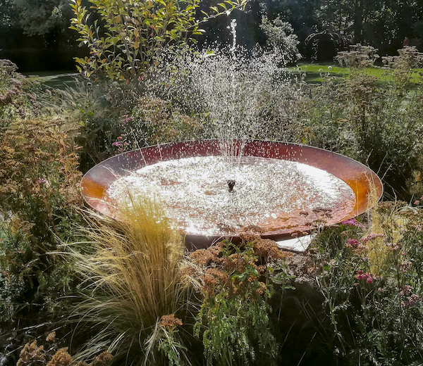 Fontaine en acier Corten de Kubik Création au coeur d'un jardin florissant