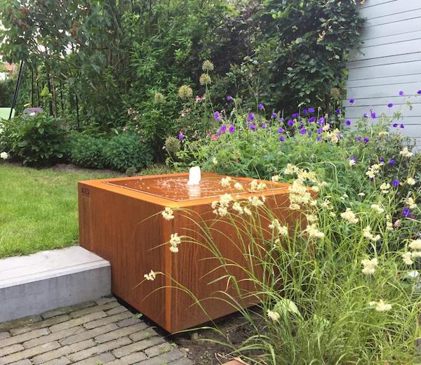 Table d'eau en acier Corten de Kubik Création entourée de fleurs sauvages dans un jardin